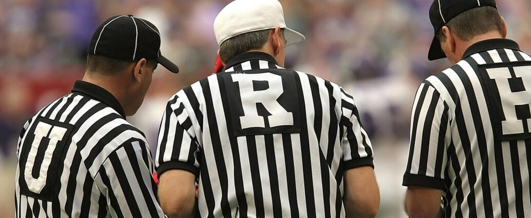 Three referees in black and white striped uniforms at a sports event.