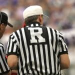 Three referees in black and white striped uniforms at a sports event.