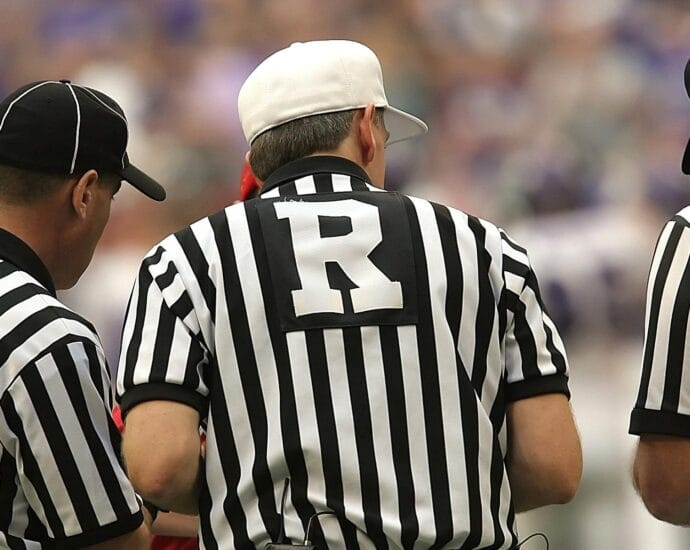 Three referees in black and white striped uniforms at a sports event.