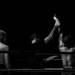 Black and white image capturing a victorious boxing moment in the ring.