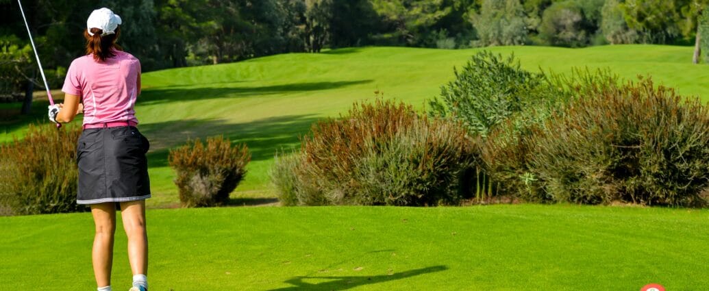 Woman playing golf on a vibrant green course with scenic tree backdrop.