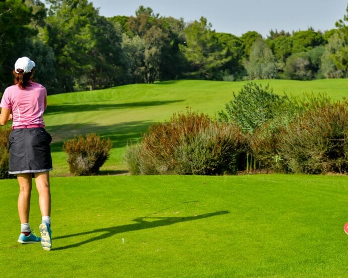 Woman playing golf on a vibrant green course with scenic tree backdrop.