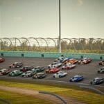 High-speed NASCAR race featuring multiple cars on a sunny day in Miami.