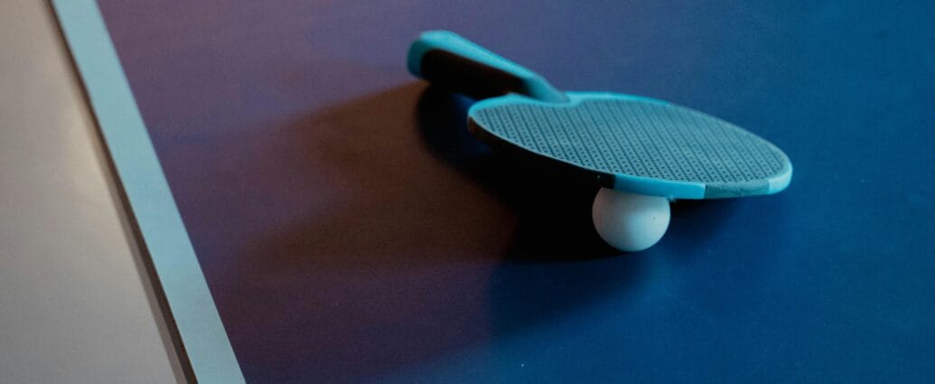Close-up of a table tennis paddle and ball on a blue table, indoor setting.