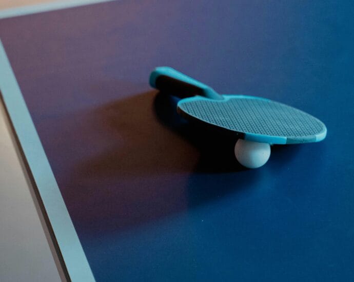 Close-up of a table tennis paddle and ball on a blue table, indoor setting.
