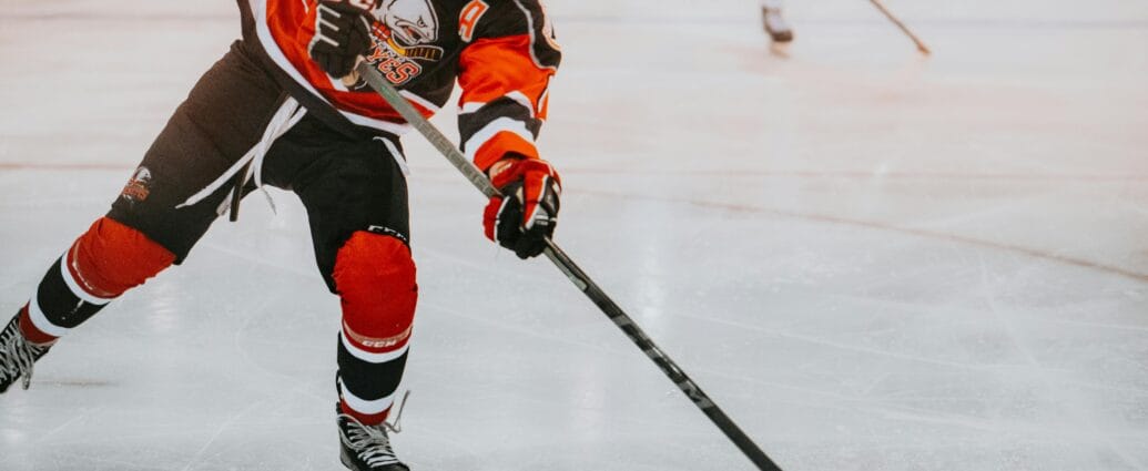 A male ice hockey player in full gear skates aggressively on ice during a game.