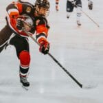 A male ice hockey player in full gear skates aggressively on ice during a game.