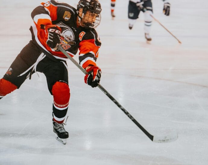A male ice hockey player in full gear skates aggressively on ice during a game.