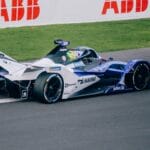 A Formula E race car speeds on track at a racing event in Mexico City, showcasing high-tech engineering.
