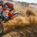 Dynamic motocross scene with rider kicking up dust on a dirt track.