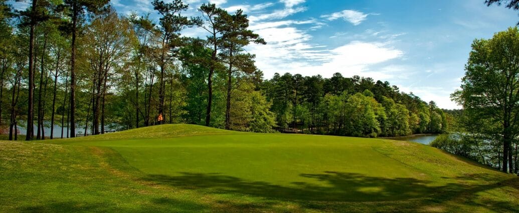 Beautiful golf course surrounded by trees and lake under a clear blue sky.