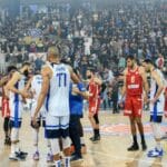 Basketball players in action during a competitive match with a full stadium crowd.