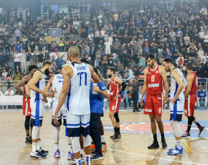 Basketball players in action during a competitive match with a full stadium crowd.