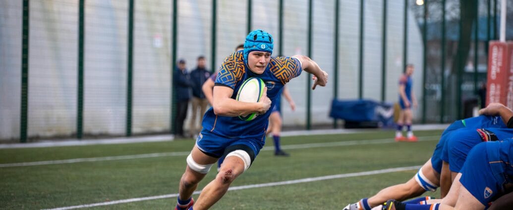 Dynamic rugby action shot featuring a player running with the ball at a match in Manchester, England.