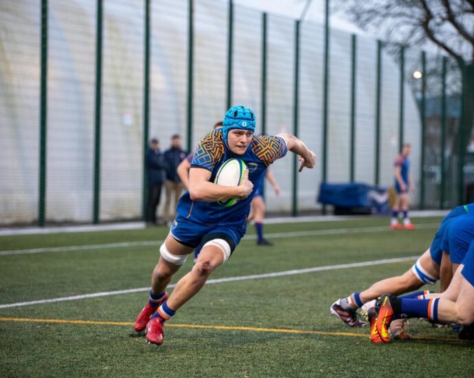 Dynamic rugby action shot featuring a player running with the ball at a match in Manchester, England.