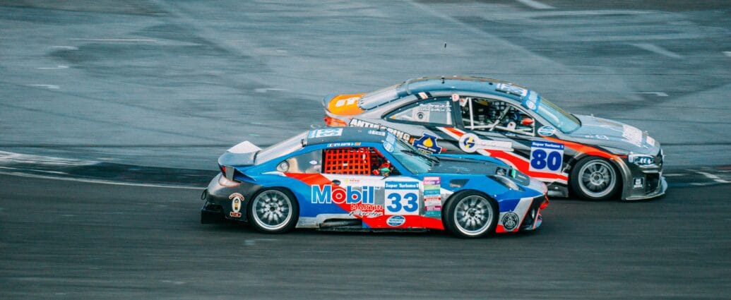 Two high-speed cars racing closely on an asphalt track during a thrilling event.