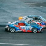Two high-speed cars racing closely on an asphalt track during a thrilling event.