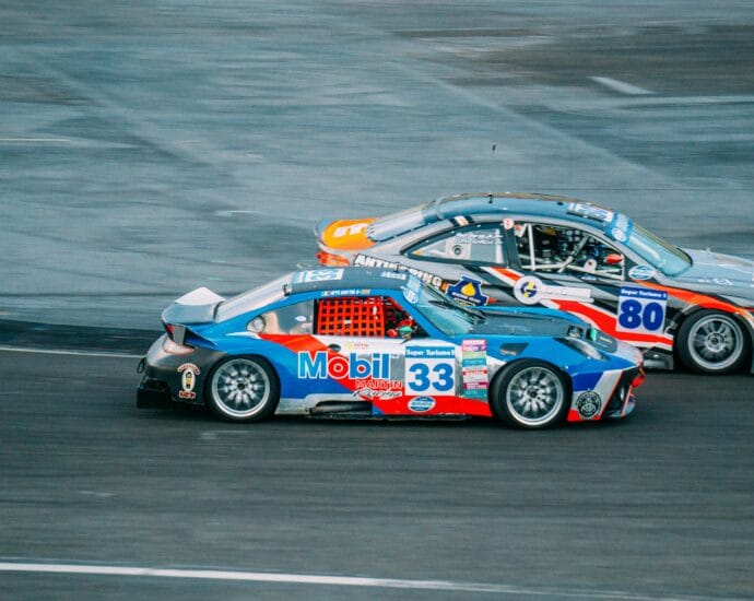Two high-speed cars racing closely on an asphalt track during a thrilling event.