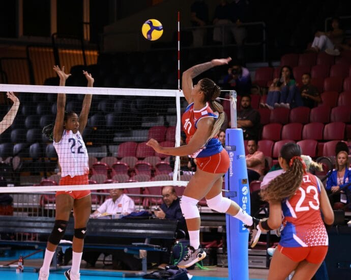Dynamic action shot from a women's volleyball match with players in mid-air at the net.