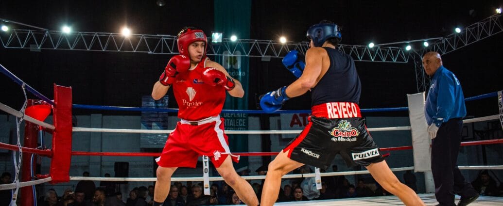 Two amateur boxers in a heated match inside a professional boxing ring.