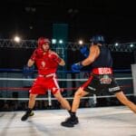 Two amateur boxers in a heated match inside a professional boxing ring.