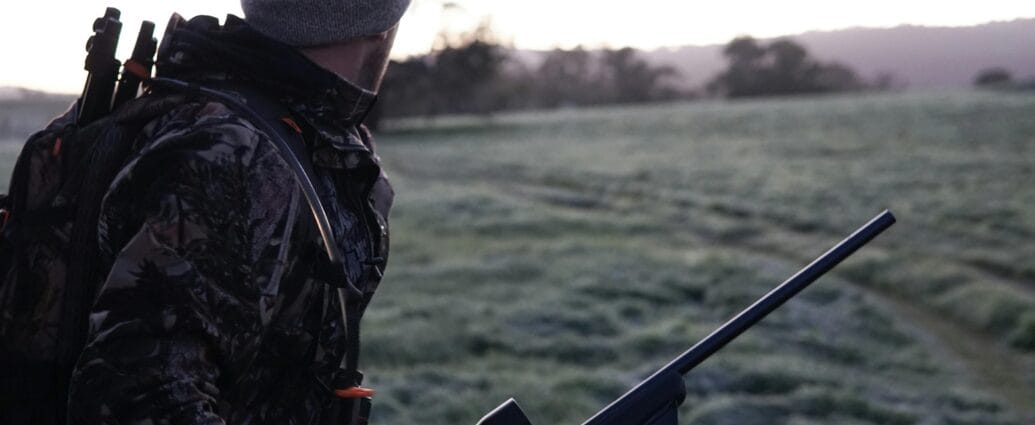 Camouflaged hunter surveying the landscape with rifle at dawn in Victoria, Australia.