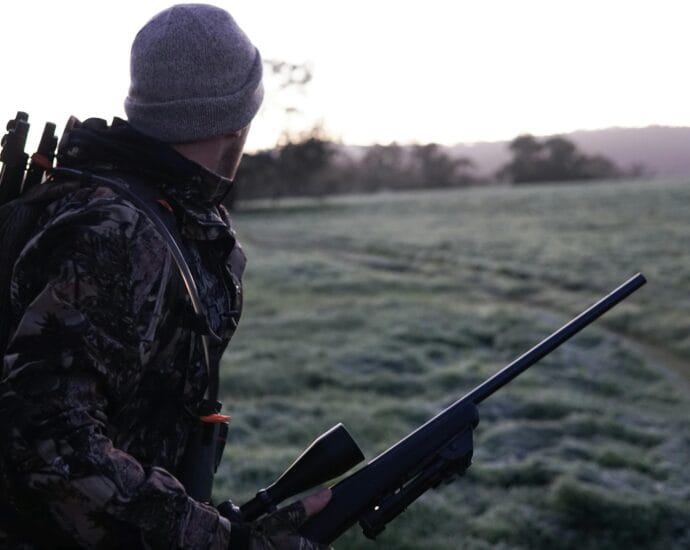 Camouflaged hunter surveying the landscape with rifle at dawn in Victoria, Australia.