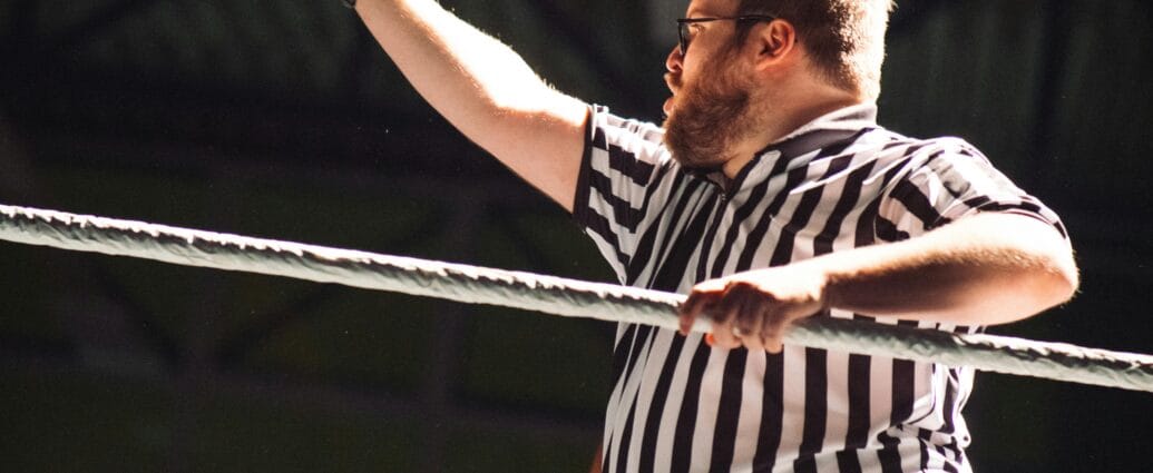 Referee signaling during an intense wrestling match, indoors.
