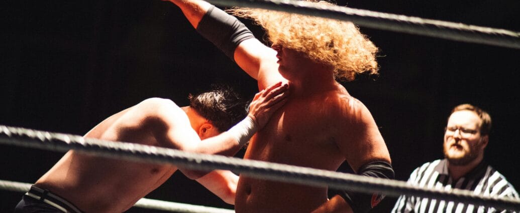 Dramatic wrestling scene with referee coaching competitors in the ring.