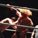 Dramatic wrestling scene with referee coaching competitors in the ring.