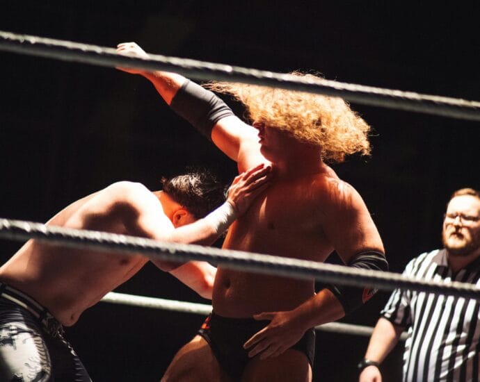 Dramatic wrestling scene with referee coaching competitors in the ring.