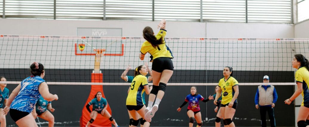 Dynamic shot of a volleyball player jumping for a spike in an indoor game. Vibrant team uniforms add energy.