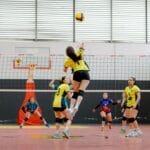 Dynamic shot of a volleyball player jumping for a spike in an indoor game. Vibrant team uniforms add energy.