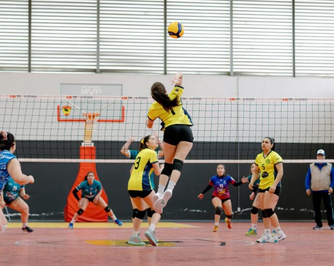 Dynamic shot of a volleyball player jumping for a spike in an indoor game. Vibrant team uniforms add energy.