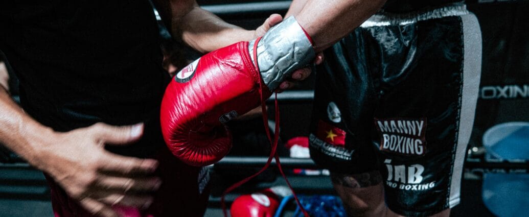 Boxer getting ready for a fight with trainer's help, showcasing red gloves and black shorts.