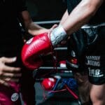 Boxer getting ready for a fight with trainer's help, showcasing red gloves and black shorts.