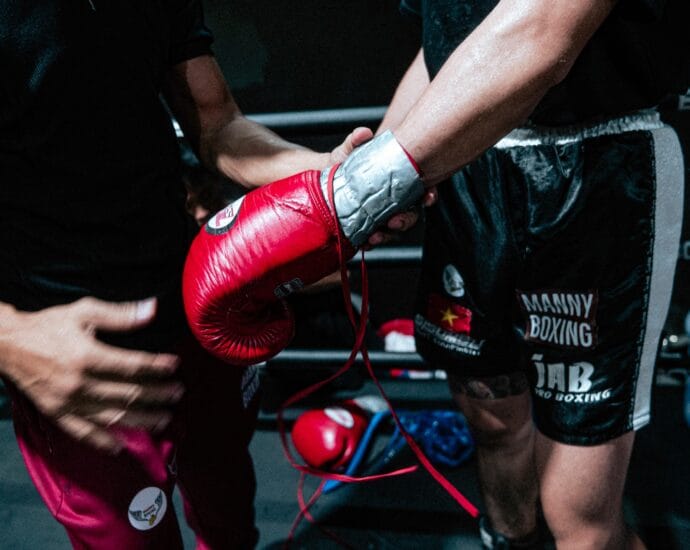Boxer getting ready for a fight with trainer's help, showcasing red gloves and black shorts.