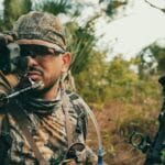 Hunter in camouflage gear using a rangefinder while outdoors, showcasing focus and precision.