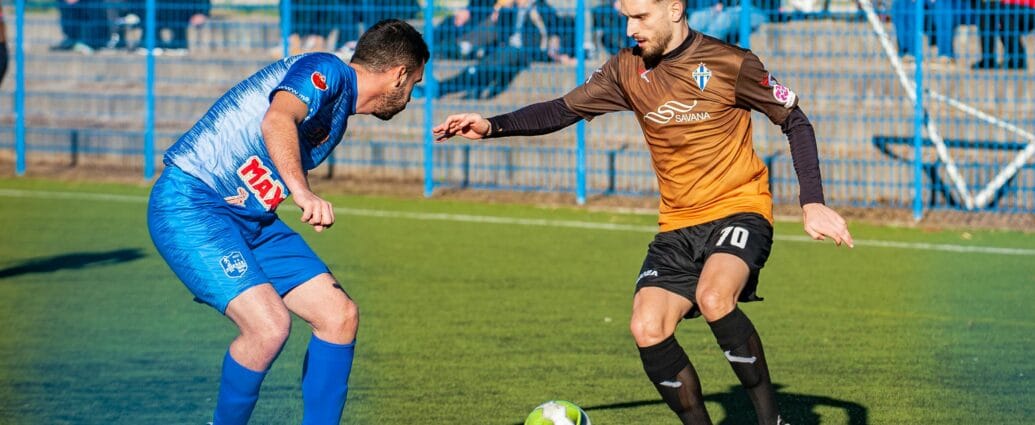 Two male soccer players in action during a competitive match on a grass field.