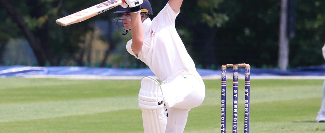 Cricketer in action performing a sweep shot on a sunny outdoor pitch.