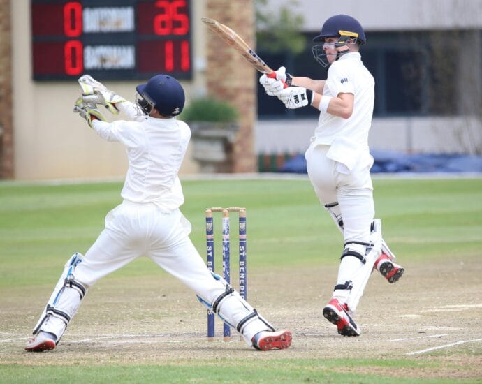 Dynamic cricket scene with batsman playing a shot and wicketkeeper in action.