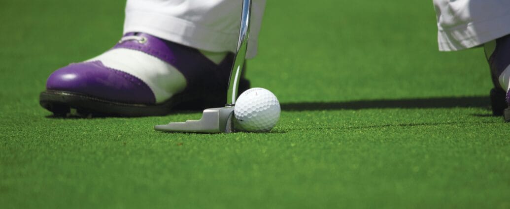 A golf player prepares to hit a ball with a putter on a green course.