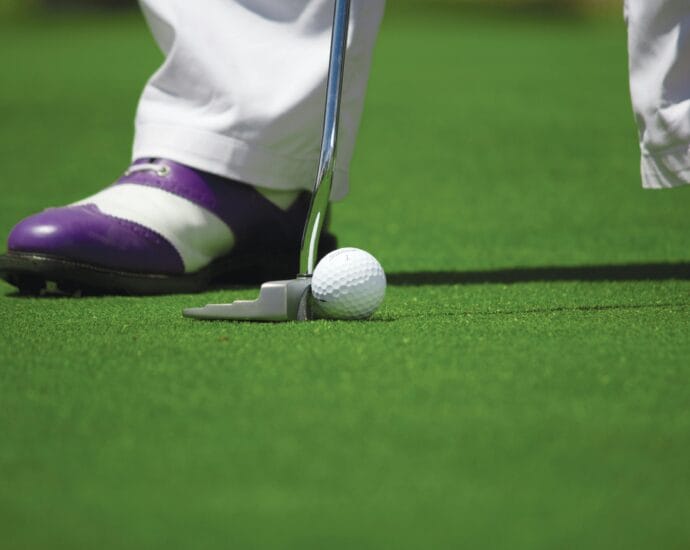 A golf player prepares to hit a ball with a putter on a green course.