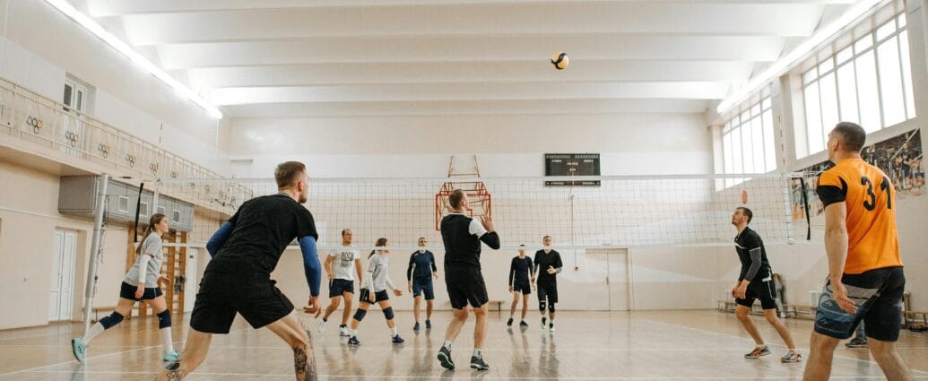 Indoor volleyball match featuring mixed-gender teams actively playing and competing.