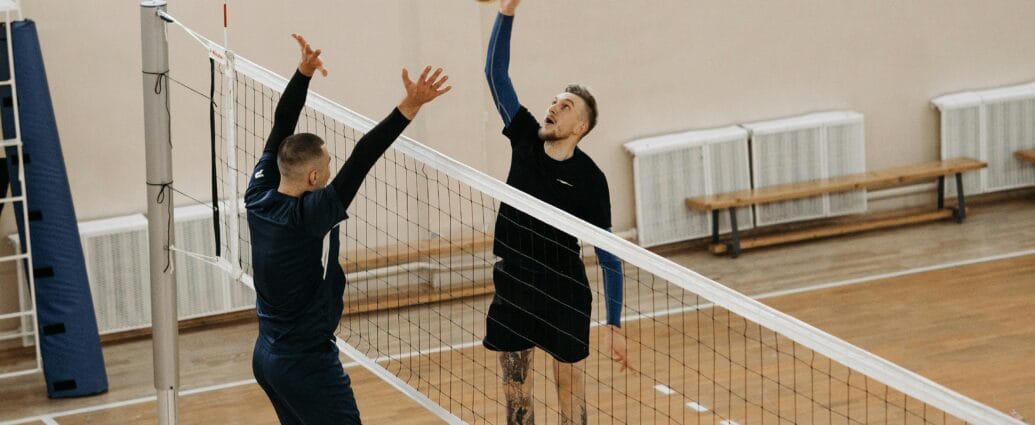 Two male athletes playing a competitive volleyball game indoors.