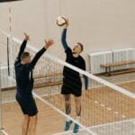 Two male athletes playing a competitive volleyball game indoors.