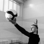 Caucasian man serving a volleyball in an indoor game setting, black and white photo.