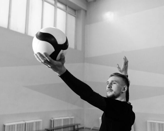 Caucasian man serving a volleyball in an indoor game setting, black and white photo.