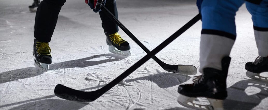 Close-up of hockey players battling for puck during an intense face-off on a lighted ice rink.