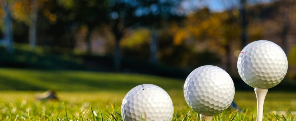 Three golf balls on tees ready for play on a bright sunny day in a green field.